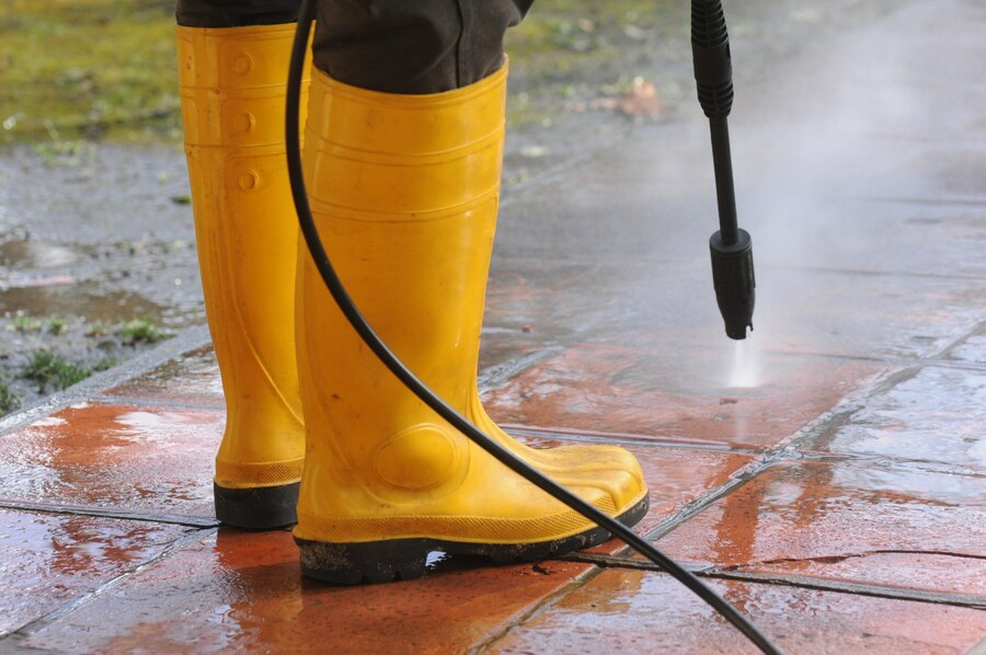 pessoa de botas em PVC amarelo lavando lonas com uma lavadora de alta pressão